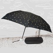 A black DrizzlePro umbrella with small gold musical note patterns is open next to its black zippered case on a sketched