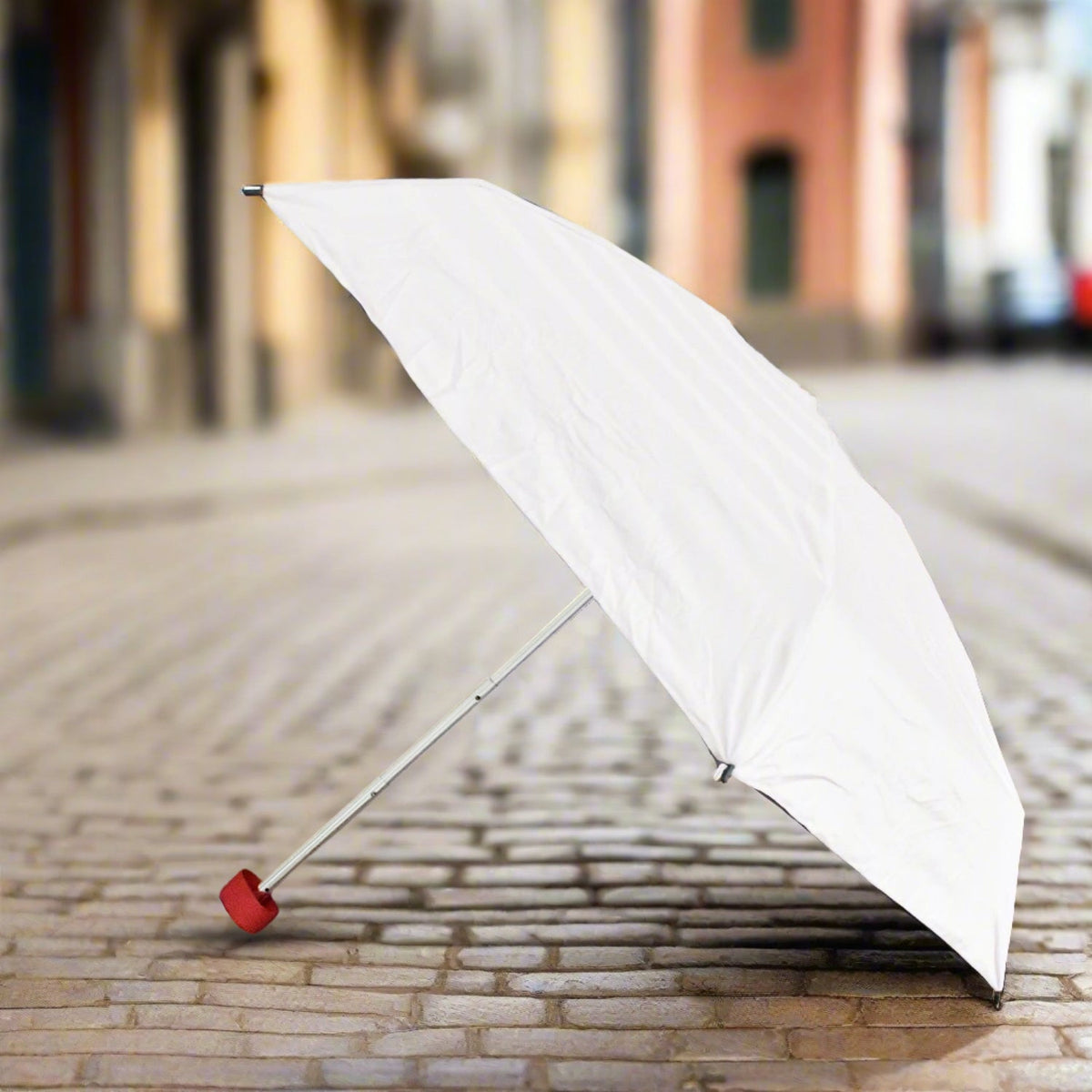 A white umbrella with a red handle stands open on a cobblestone street, ready for use.
