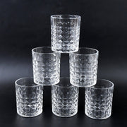 Three diamond-cut glass tumblers filled with different beverages on a wooden surface, ready for serving.
