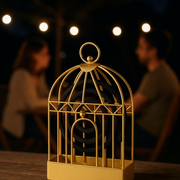 A gold birdcage-style holder with a mosquito coil sits on a wooden table, with two blurred figures and string lights in the