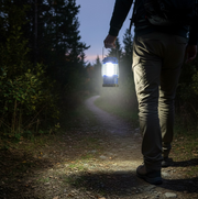 A person walks away on a dark, winding path, holding a blue and black LED lantern that lights the way.