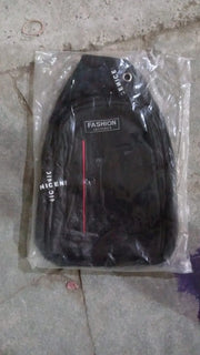 A black sling bag with a red stripe and 'FASHION' label is sealed in clear plastic packaging on a floor.