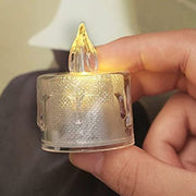 A hand gently holding a single transparent flameless LED tea light candle.