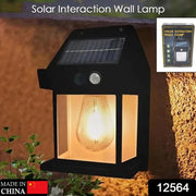 A black solar wall lamp with a glowing bulb is on a brown wall, with a small product box in the top right corner.