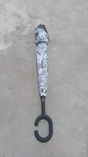 A closed reverse umbrella with a black and white newspaper print is standing upright on a grey concrete surface.